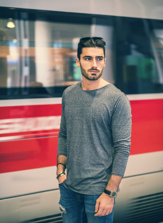 Handsome young male traveler in train station with moving train behind him, looking to a sideの写真素材