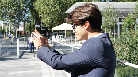 Handsome young man in city setting, taking photos with cell phone
