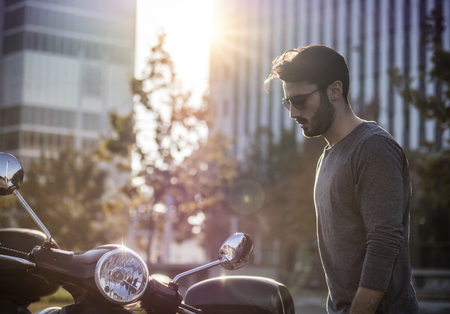 Young handsome man sitting on scooter in backlit on city street.の写真素材