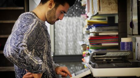 Handsome young man in jumper standing near photocopier and using it.の写真素材