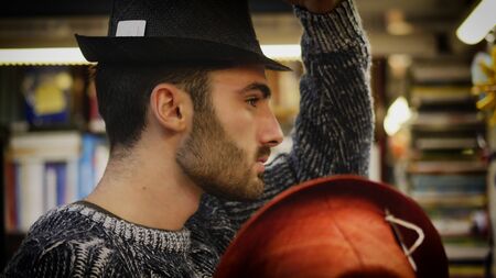 Handsome young man standing in shop and trying different hats on.の写真素材