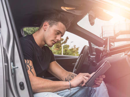 Handsome young man in casual clothes sitting in his car and using tablet PC.の写真素材