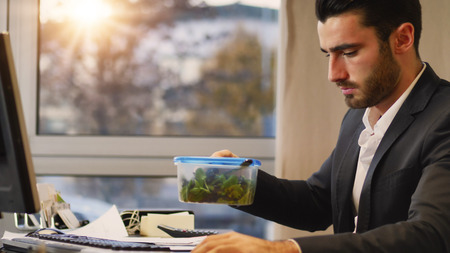 Elegant man in suit having lunch at table in office while talking on phone and watching computer.の写真素材