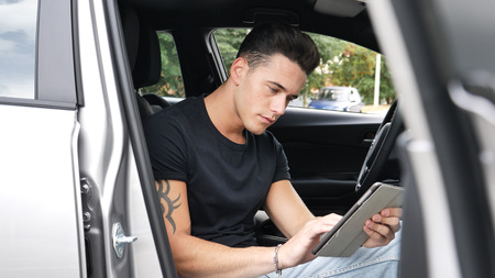 Handsome young man in casual clothes sitting in his car and using tablet PC.の写真素材