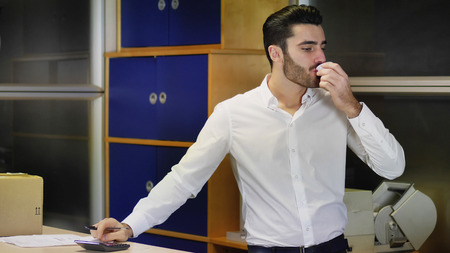 Handsome young businessman in white shirt standing at counter in office, receiving cup of coffee from colleague while working on documentsの写真素材
