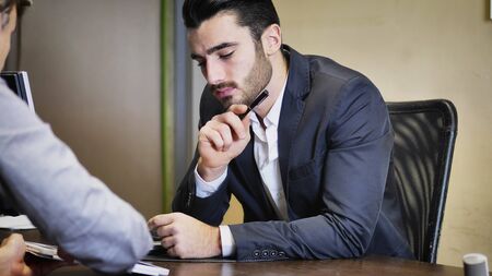 Handsome businessman sitting in his office, talking to client and showing him options on tablet PC...