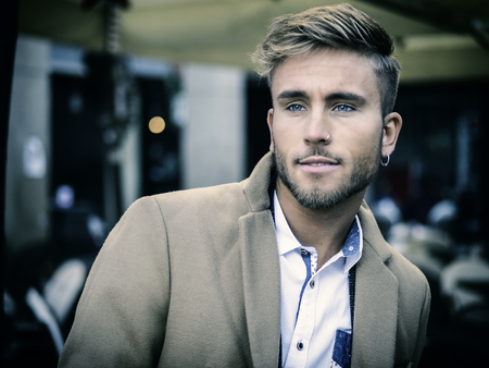 Handsome trendy blond man standing outdoor in European city setting with elegant old historic...