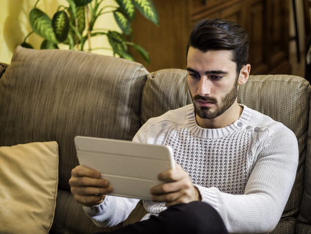 Handsome young man sitting indoors video chatting with tablet PC, smiling for the webcameraの写真素材
