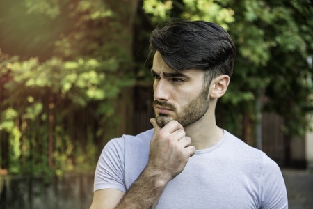 Confused or doubtful young man scratching his head and looking up. Outoodr on the street