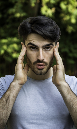 Frustrated young man with headache, covering temples with handsの写真素材