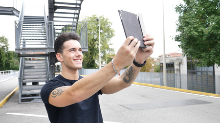 Portrait of young attractiave man in business suit using tablet PC to take selfie photo outside in city streetの写真素材