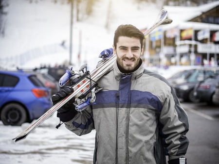 Young handsome man in sportswear holding ski and looking at camera smilingの写真素材