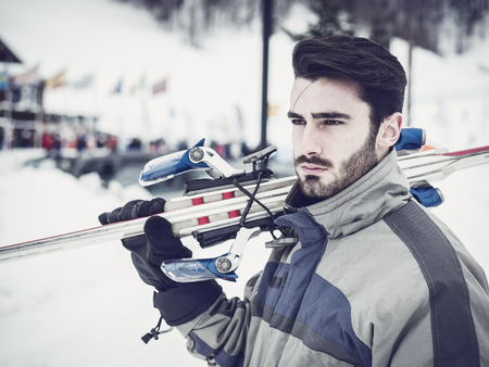 Young handsome man in sportswear holding ski on shoulder and looking away.の写真素材