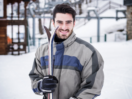 Young handsome man in sportswear holding ski and looking at camera smiling