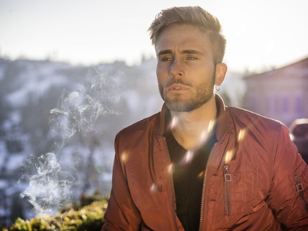 Handsome young man outdoor in winter fashion, wearing black coat and woolen scarf in city parkの写真素材