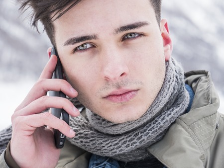 Handsome young man making a call with smarpthone while standing at snowy mountainの写真素材