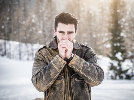 Handsome young man in jacket having cold hands while looking confidently at camera in nature.の写真素材