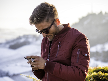 Handsome young man outdoor in winter fashion using smartphone to send text message or surf the web, wearing black coat and woolen scarfの写真素材