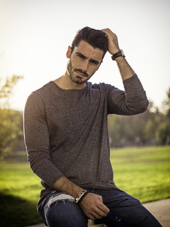 Attractive young bearded man portrait sitting outside in urban environment, looking at cameraの写真素材
