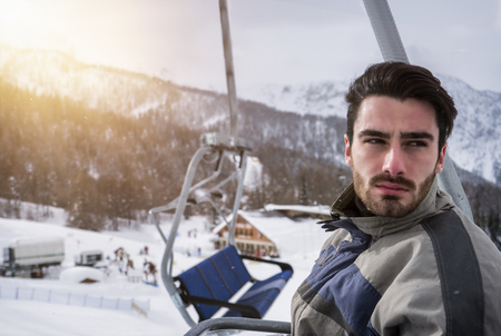 Portrait of handsome man in skiing suit sitting on chairlift rising up and looking at camera.の写真素材