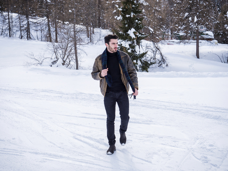 Stylish man walking confidently looking away on territory of contemporary winter resort covered in snow in the mountainの写真素材