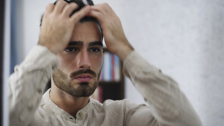 Sad, upset young man at home, with hands on his head, thinking worried
