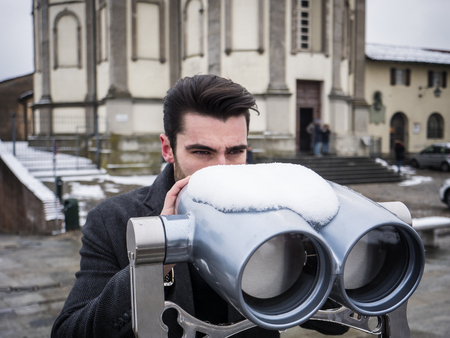 Back view of unrecognizable stylish man watching sights through binoculars in winter in Turin, Italy.の写真素材