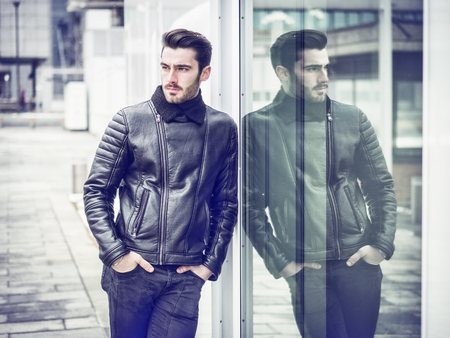 Handsome bearded young man outdoor in winter fashion, wearing black leather jacket in modern city settingの写真素材