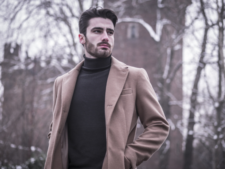 Handsome young man standing outside in winter, in snowy Turin, in Italy, in urban settingの写真素材