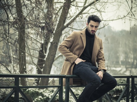 Handsome young man standing outside in winter, in snowy city park. Cold urban settingの写真素材