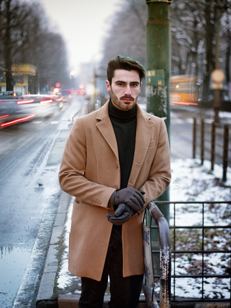 Handsome young man standing outside in winter, in snowy city. Cold urban settingの写真素材