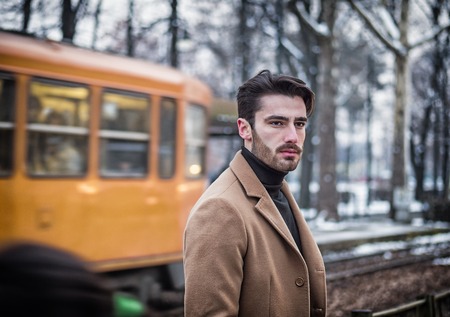Handsome young man standing outside in winter, in snowy city. Cold urban settingの写真素材