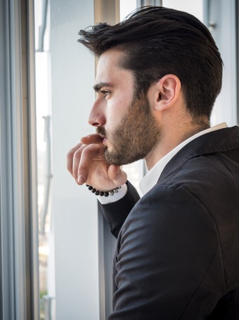 Handsome serious businessman standing inside modern building next to big window, looking outの写真素材