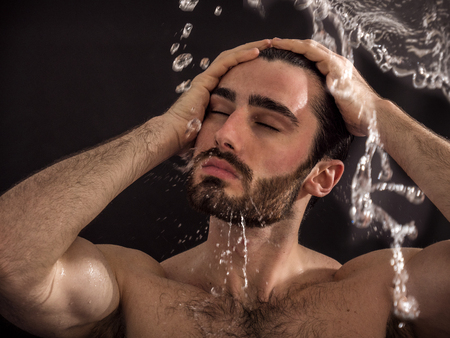 Shirtless handsome young man with water splashes on his face and chest in studio shotの写真素材