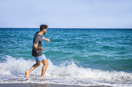 Young Handsome Man on Sandy Beach Skipping Stones on Seaの写真素材