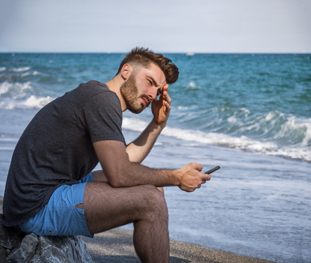 Handsome young man sitting on a beach, feeling lonely and sad or simply relaxed, shirtless wearing boxer shortsの写真素材