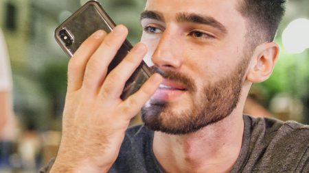 Young handsome man sending voice message outside at night sitting at bar table in a summer day in cityの写真素材