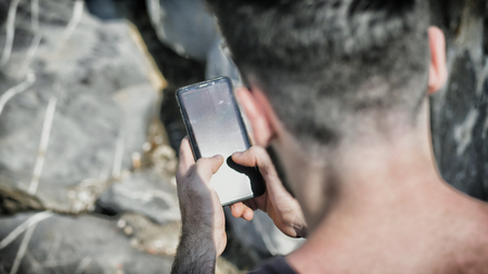 Over the shoulder shot of a young man using cell phone to send text message, on a beachの写真素材