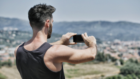 Young handsome man using smartphone to take shots and photos of the landscape at the seasideの写真素材