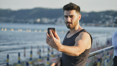 Young man at beach taking selfie photo with his cell phoneの写真素材