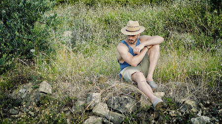 Attractive, fit young man relaxing sitting in a grass field, wearing straw hatの写真素材