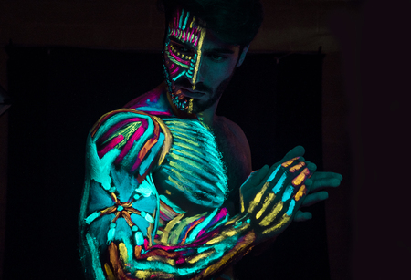Young man painted in fluorescent paint on face and muscular torso, in studio shot with UV lightの写真素材