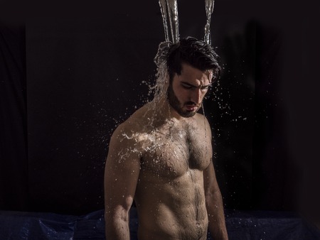 Shirtless handsome young man with water splashes on his face and chest in studio shotの写真素材