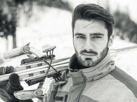 Young handsome man in sportswear holding ski and looking at camera smiling