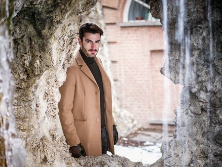 Handsome young man standing outside in winter, in snowy city park. Cold urban settingの写真素材