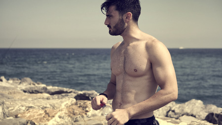 Attractive shirtless muscleman on the beach drinking water from plastic bottleの写真素材