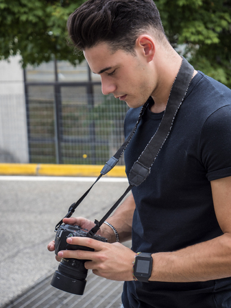 Handsome young male photographer taking photograph with professional photo camera hanging from his...