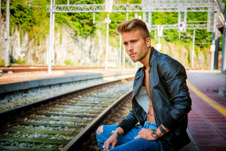 Attractive young man sitting on railroad tracksの写真素材
