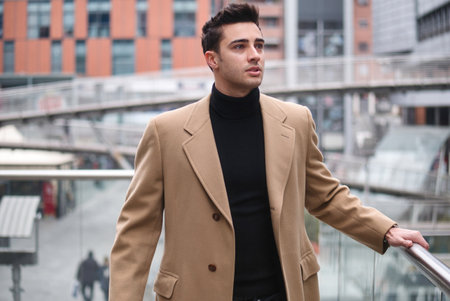 Confident young man walking in fashionable trench coat through city street.