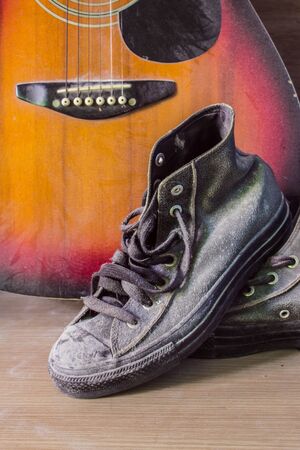 Old sneakers and guitar on the wooden floor.の写真素材